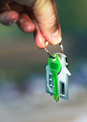 A hand holding a green key to a house