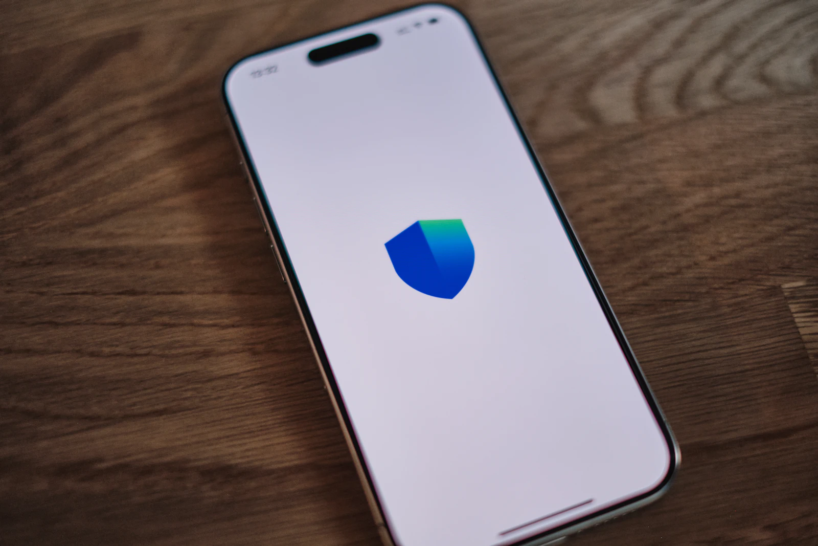 A smartphone on a wooden desk showing a blue and green security shield icon