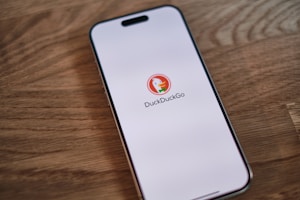 A cell phone sitting on top of a wooden table with DuckDuckGo search on screen