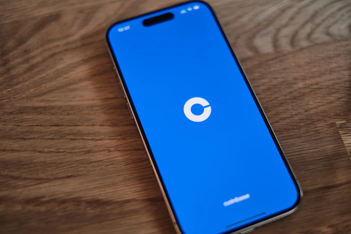 A smartphone with the Coinbase logo on a blue screen, lying on a wooden table