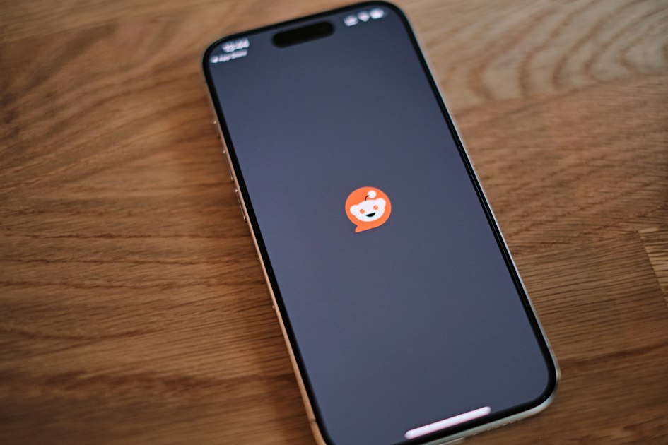 A smartphone face up on a wooden desk showing the Reddit app loading screen, its logo centred on a dark background