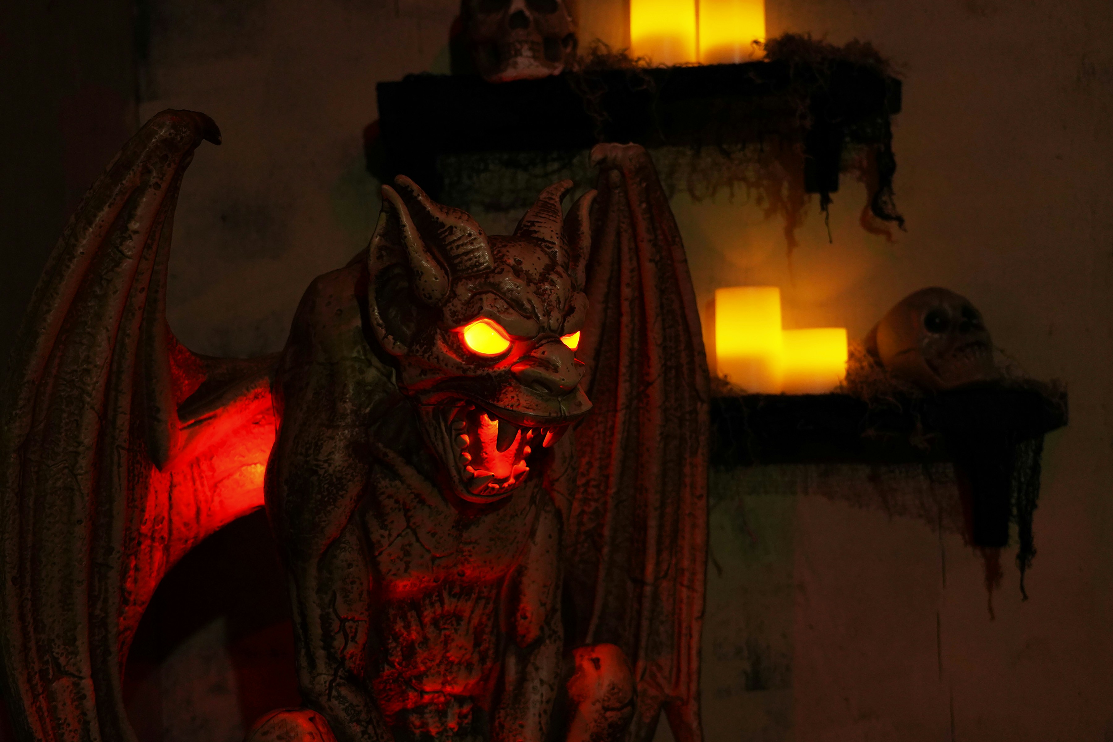 A gargoyle-like red demon with glowing yellow eyes roars in front of glowing yellow candles.