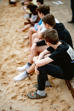 A group of kids sitting on a bench in the sand