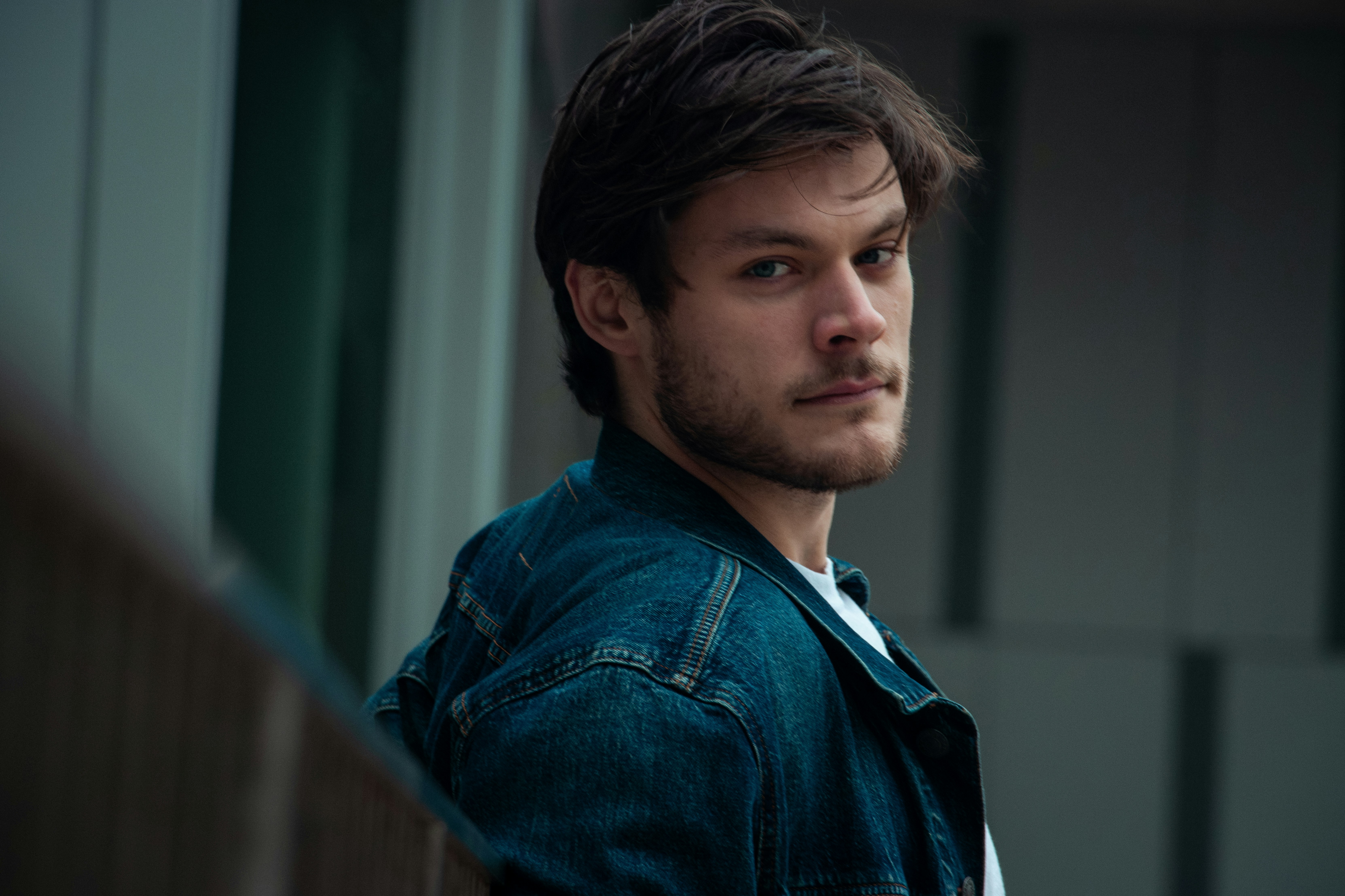 A man in a denim jacket leaning against a wall