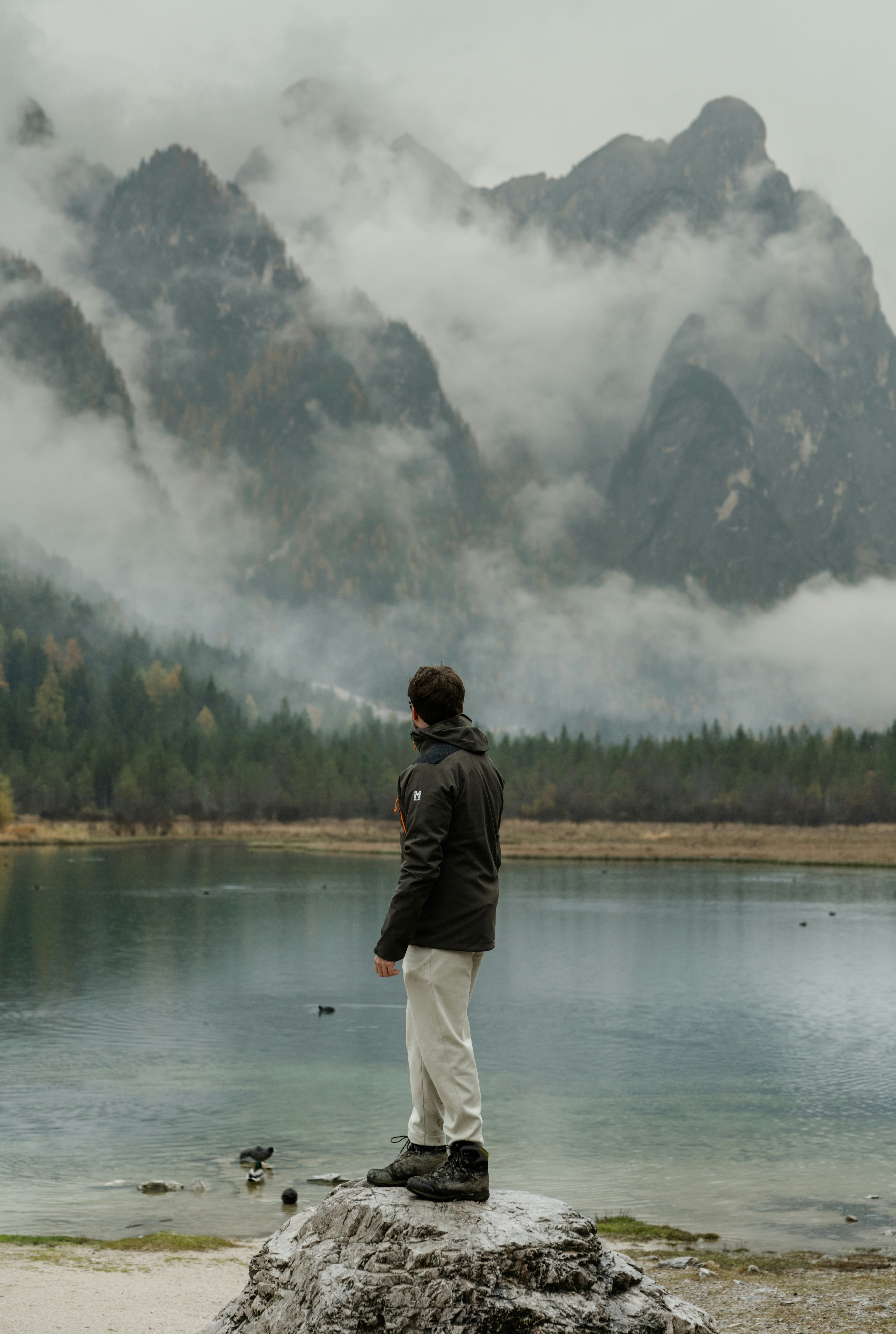 A man standing on top of a rock next to a lake