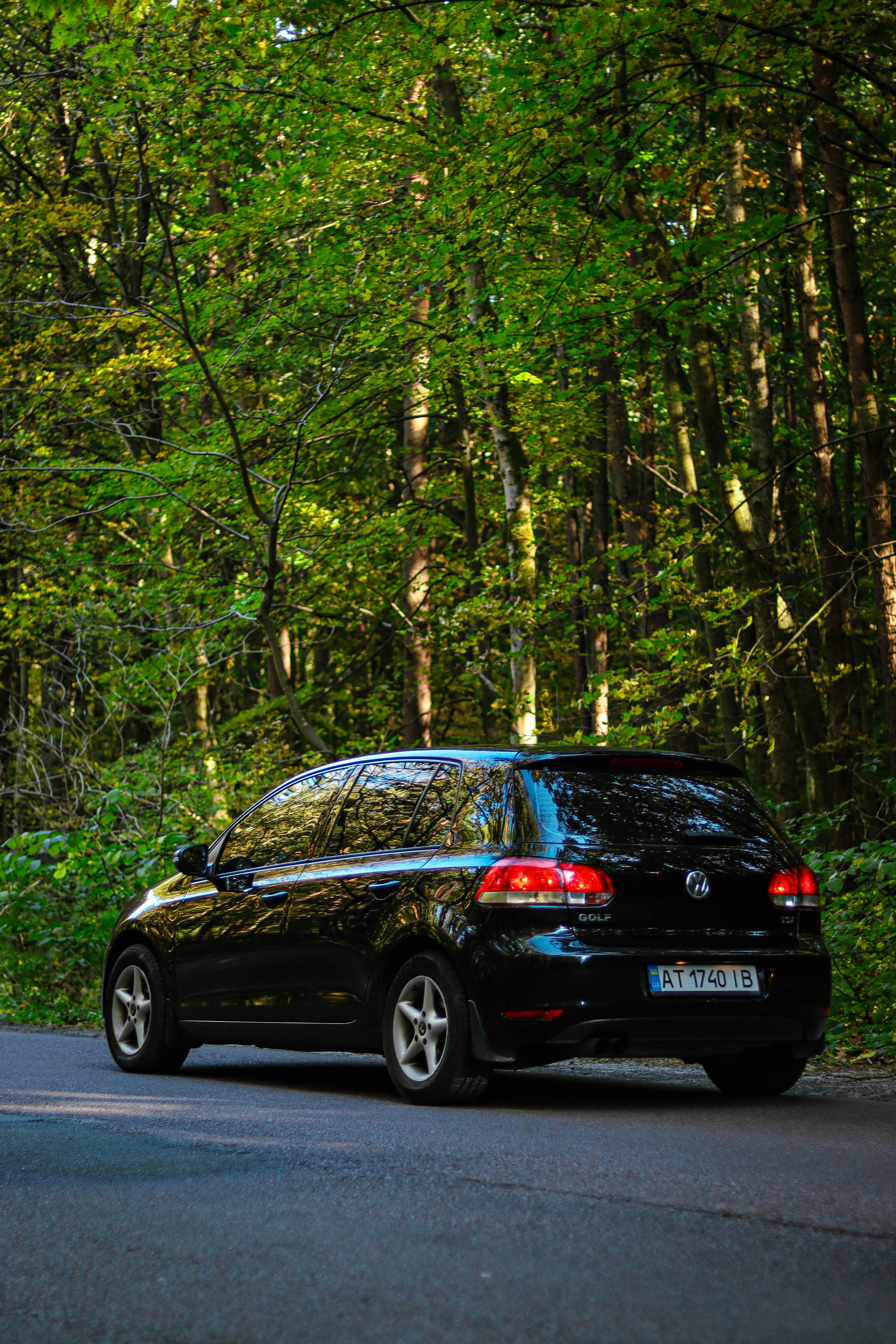 A black car driving down a road next to a forest