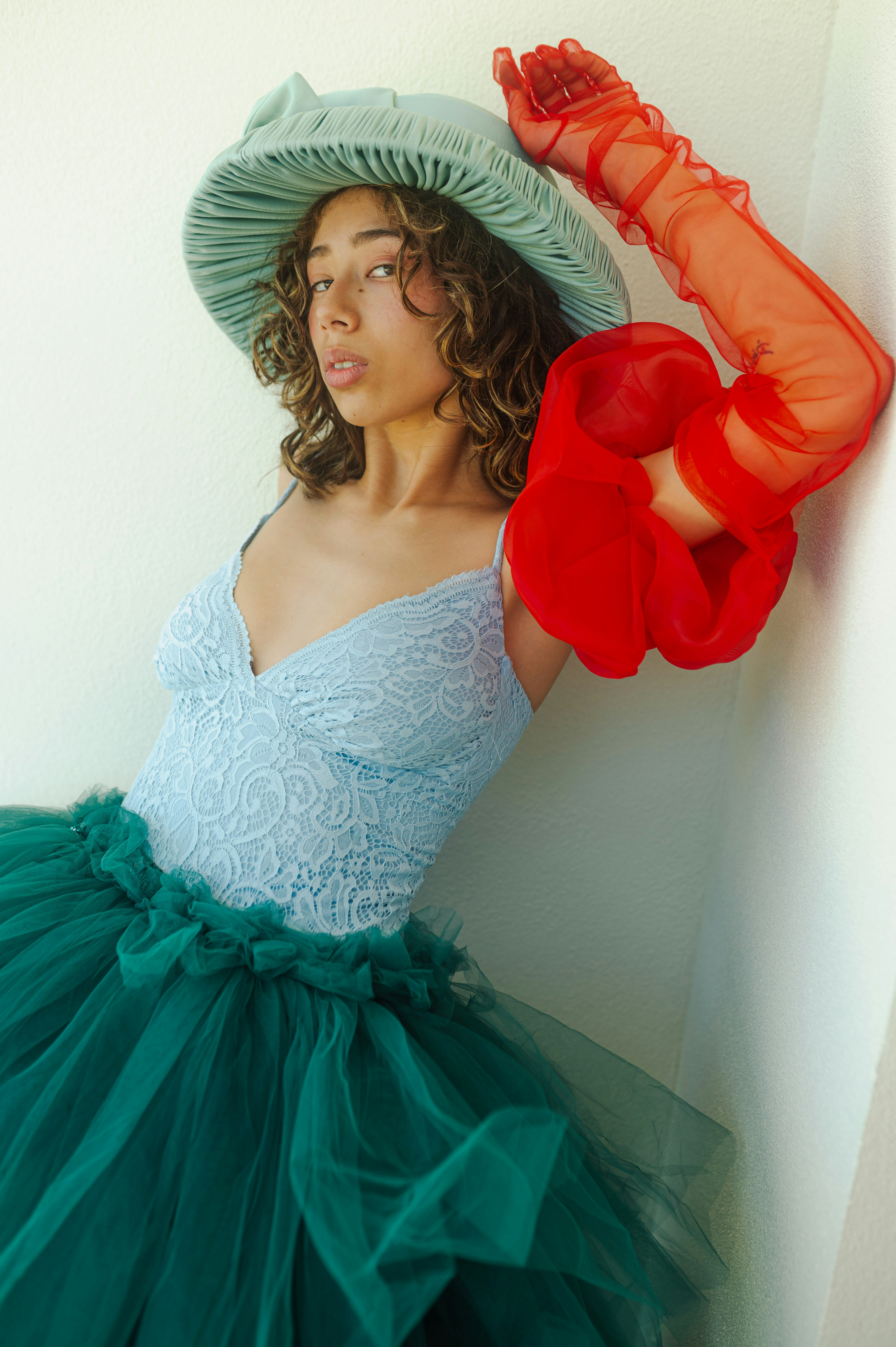 A woman in a dress and hat leaning against a wall