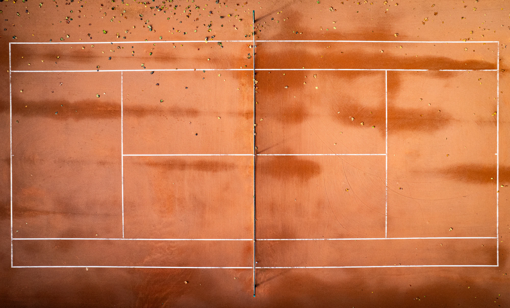 A clay tennis court with the long shadow of a single player