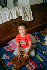 A little girl sitting on a bed with a guitar