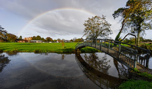 A rainbow appears over a small bridge over a pond