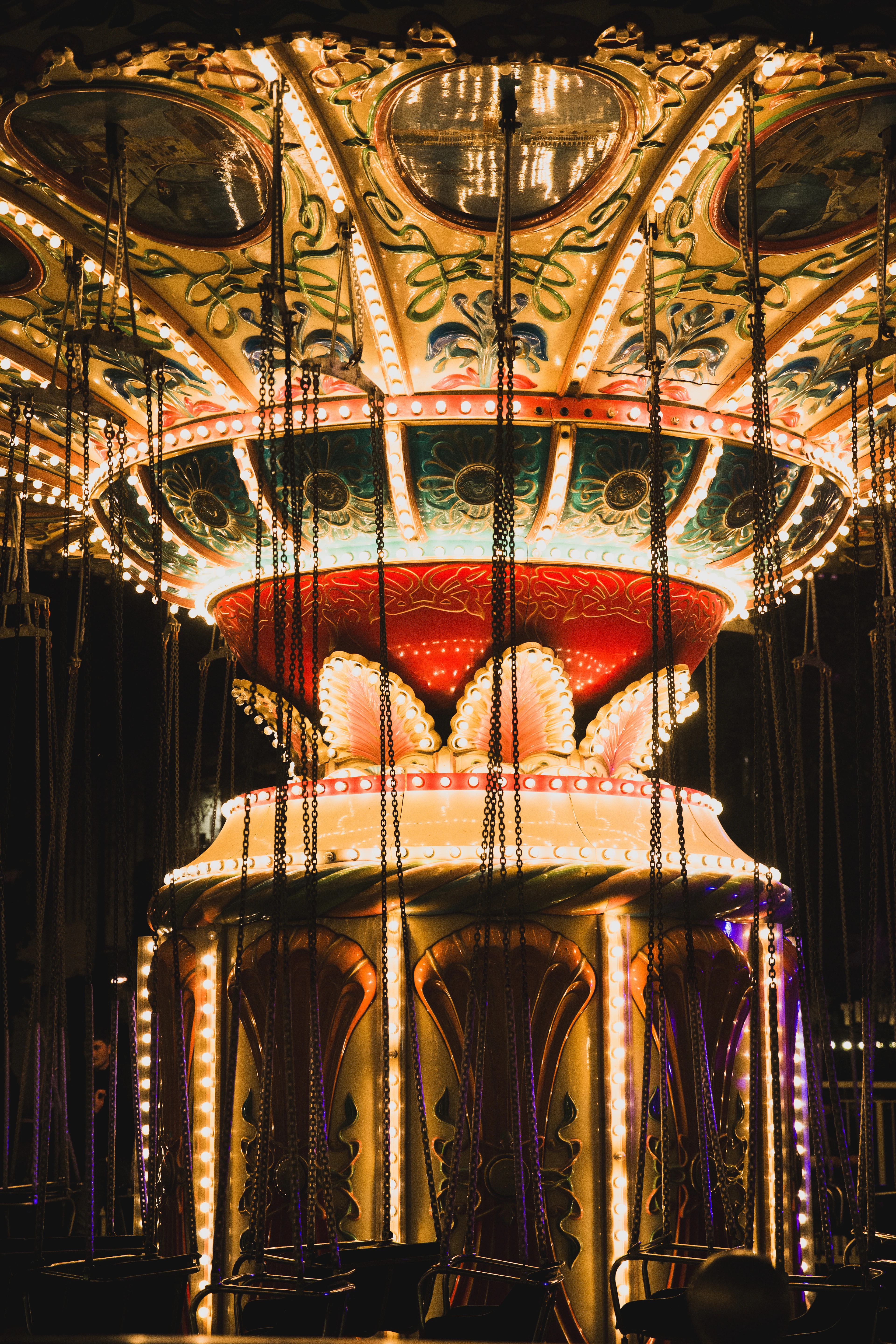 The painted canopy of Tivoli's vintage chain carousel lit by hundreds of bulbs after dark in Copenhagen, gilded panels and empty swing seats hanging on their chains in the winter night