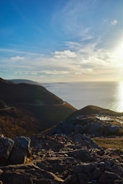 The sun is shining over the ocean on a rocky shore