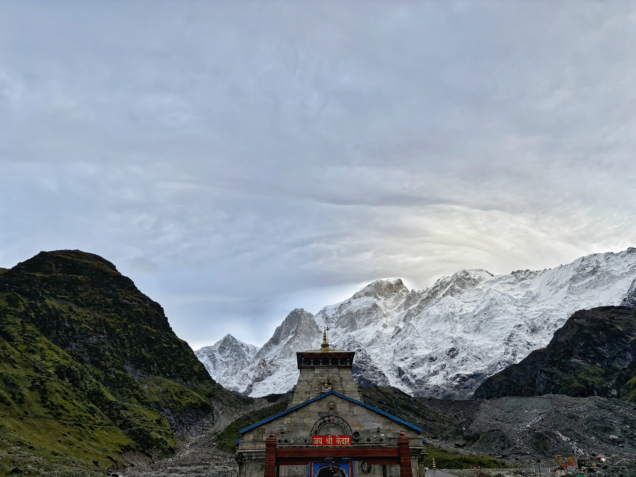 Kedarnath temple small beneath a wall of snow peaks and heavy cloud