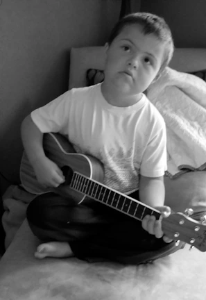 A young boy sitting on a bed playing a guitar