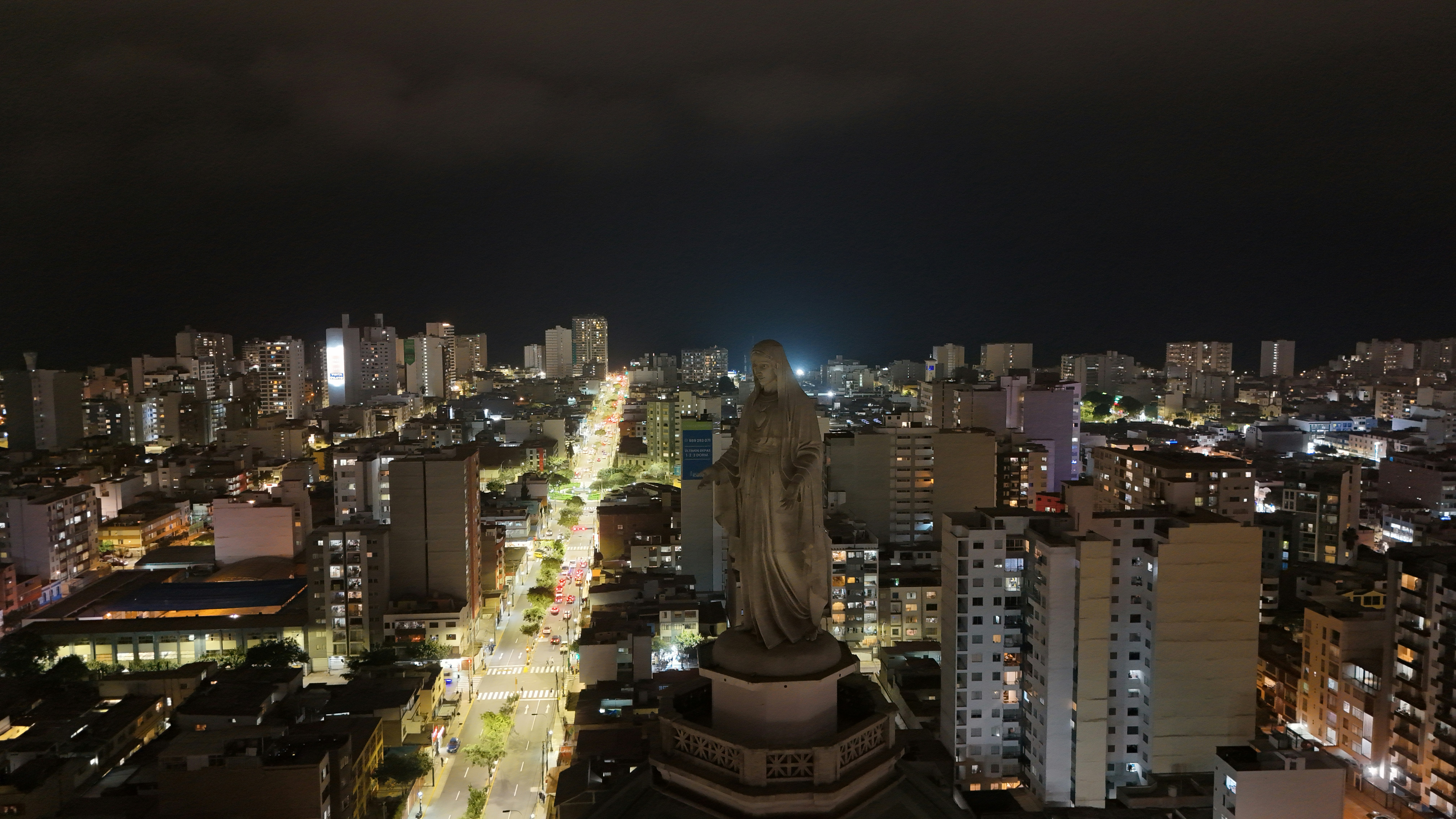 Tráfico nocturno en Lima con pantallas de noticias económicas al fondo