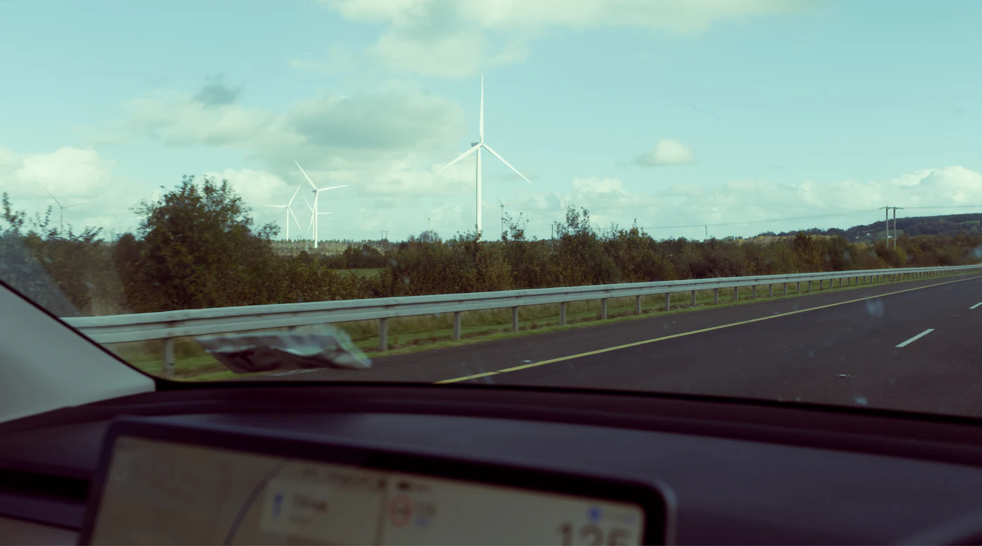 A car driving along a motorway next to a wind turbine