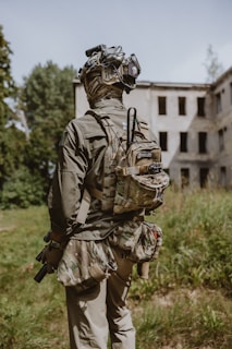 A man with a backpack and goggles standing in front of an abandoned building