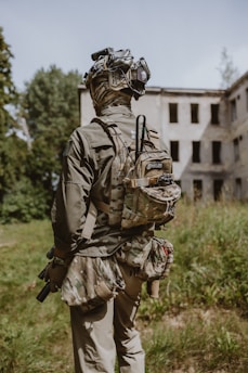 A man with a backpack and goggles standing in front of an abandoned building