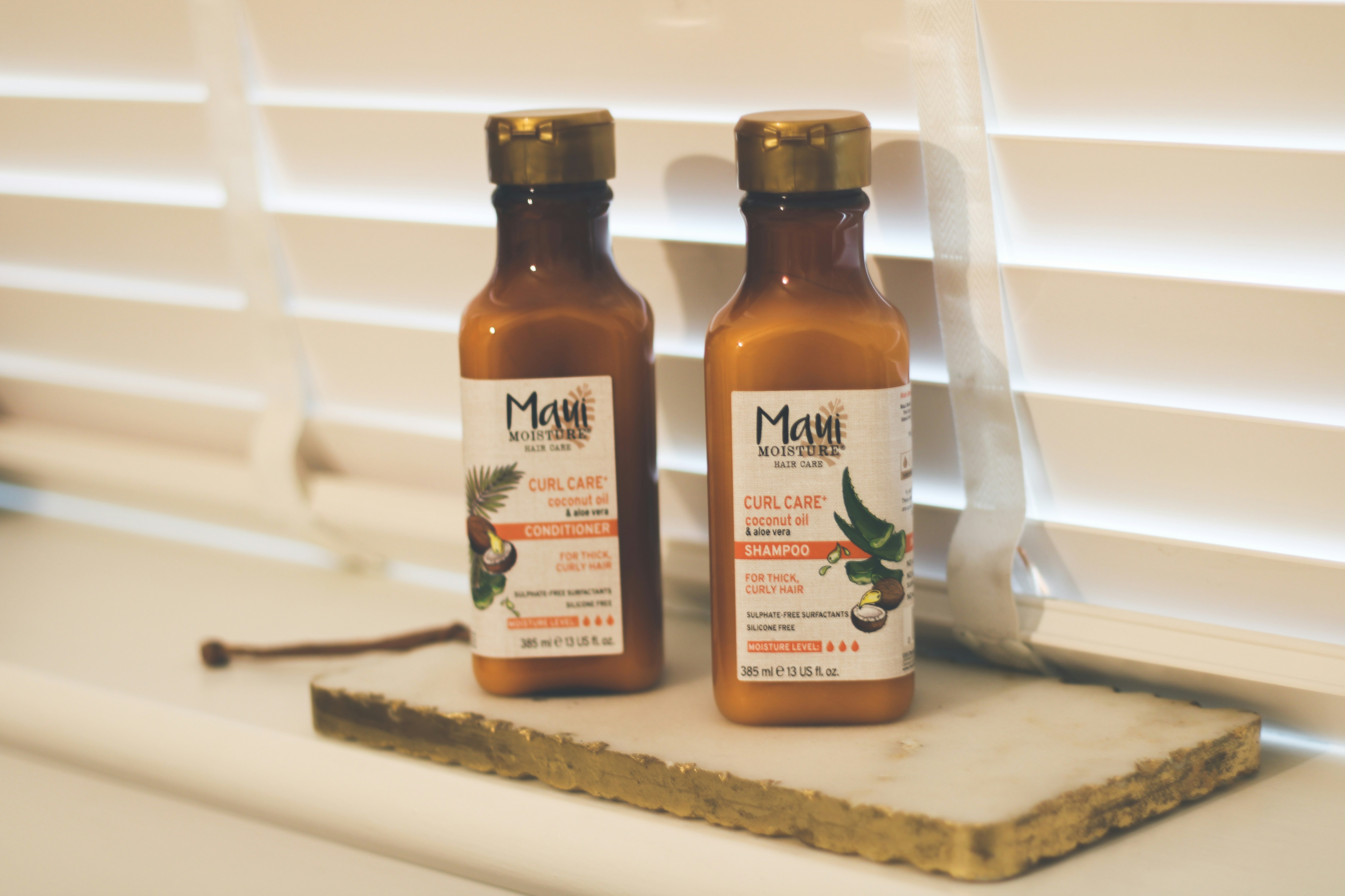 Two bottles of hot sauce sitting on a window sill