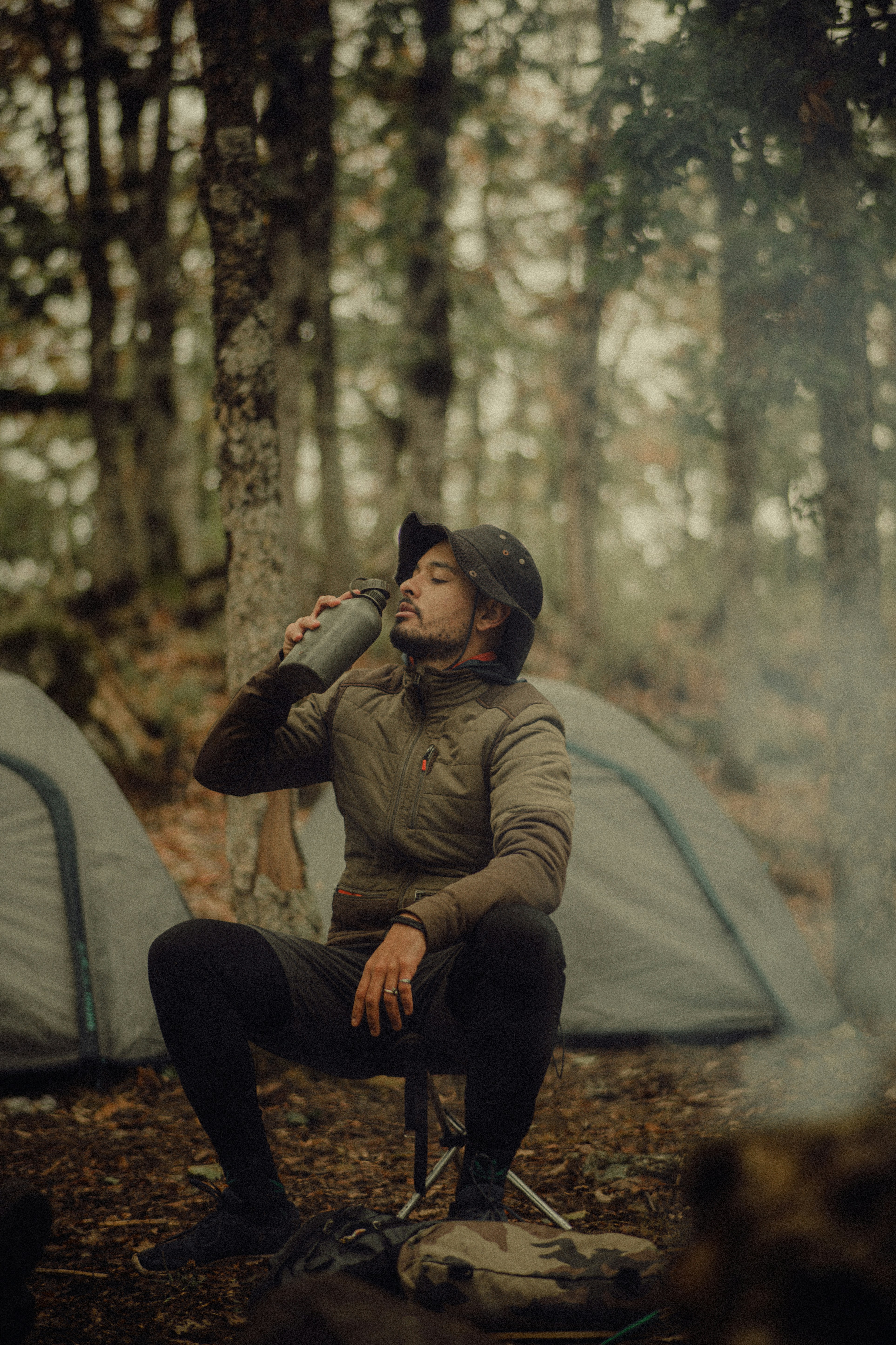 A man sitting in a chair next to a tent in the woods