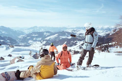 A group of people standing and sitting on top of a snow covered slope