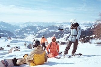 A group of people standing and sitting on top of a snow covered slope