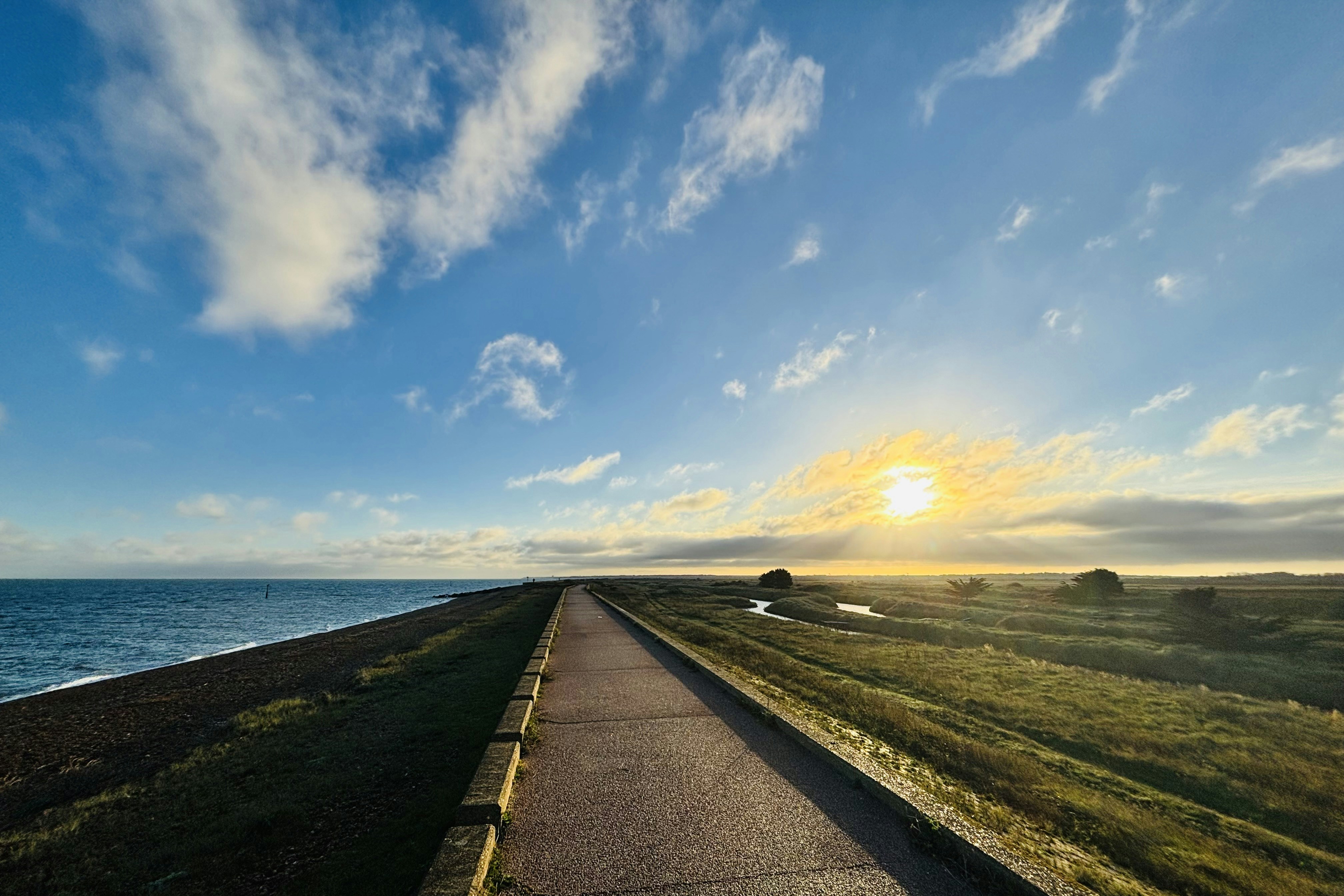The sun is setting over the ocean on the road