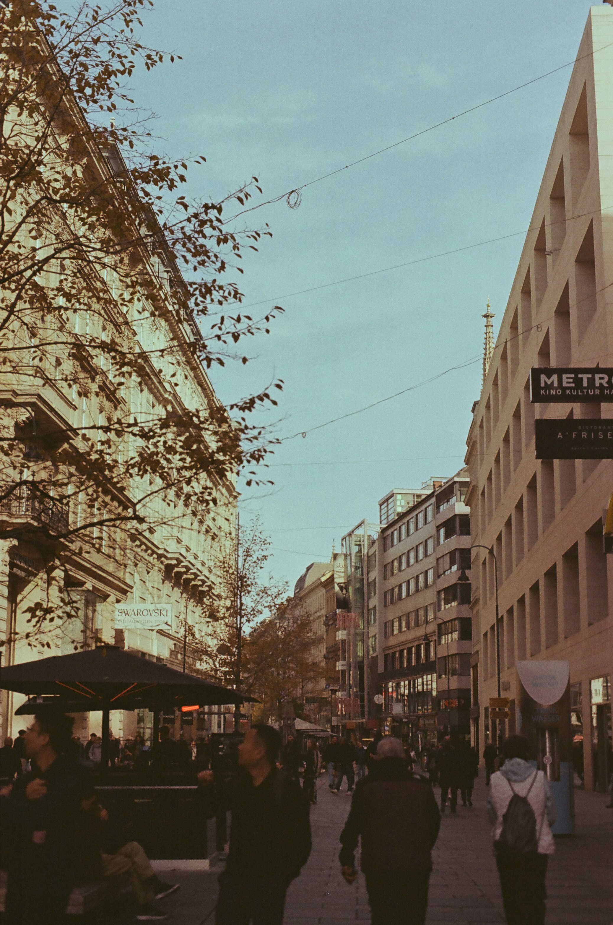 A group of people walking down a street next to tall buildings