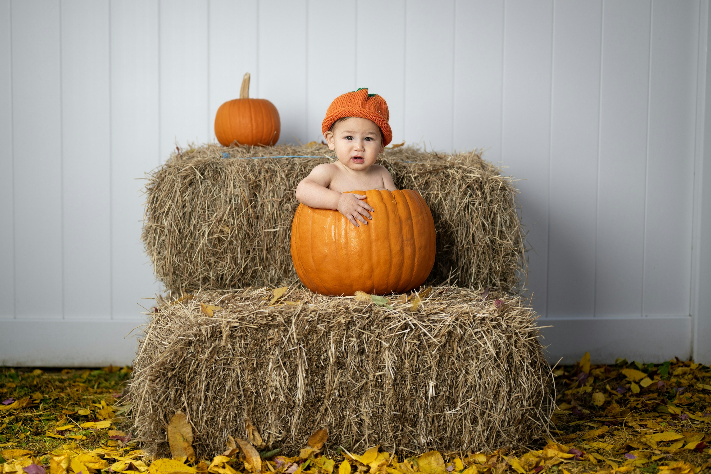 Un bébé assis sur une botte de foin avec une citrouille