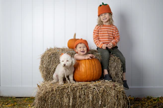 Two children sitting on a hay bale with pumpkins