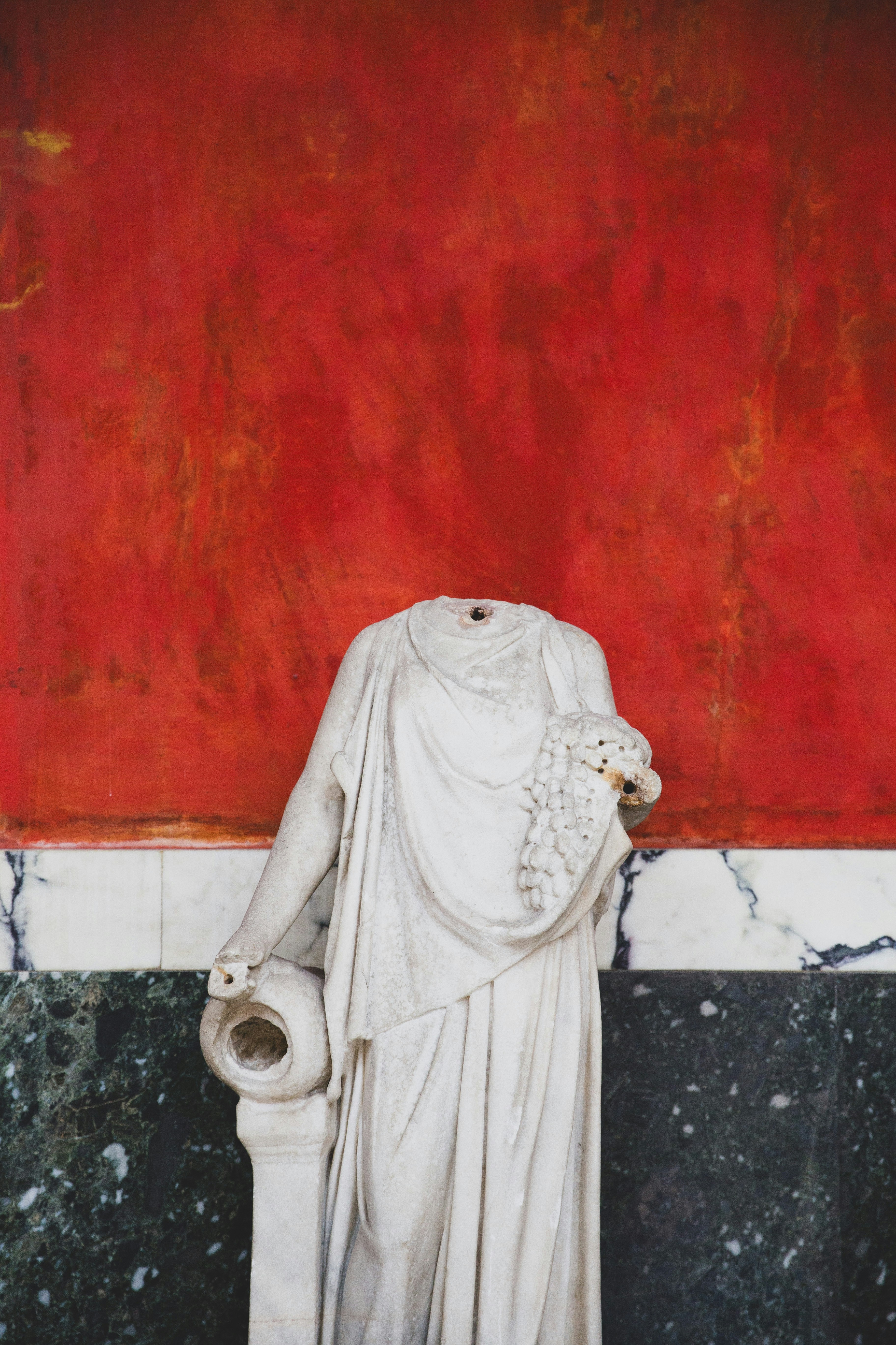 A statue of a person holding a cup in front of a red wall