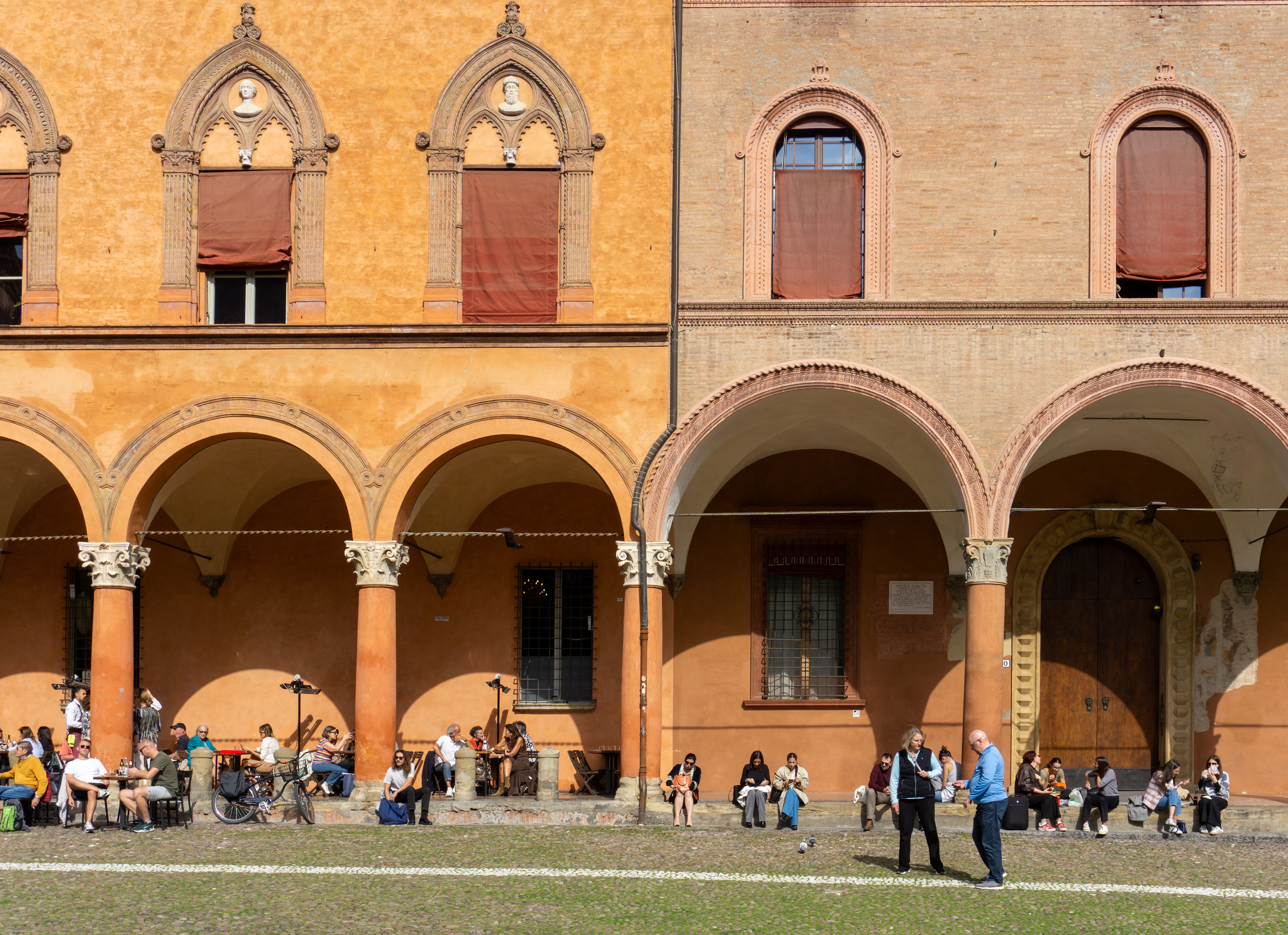 Diners under a Bologna portico, brick arches and painted vaults running the length of the street