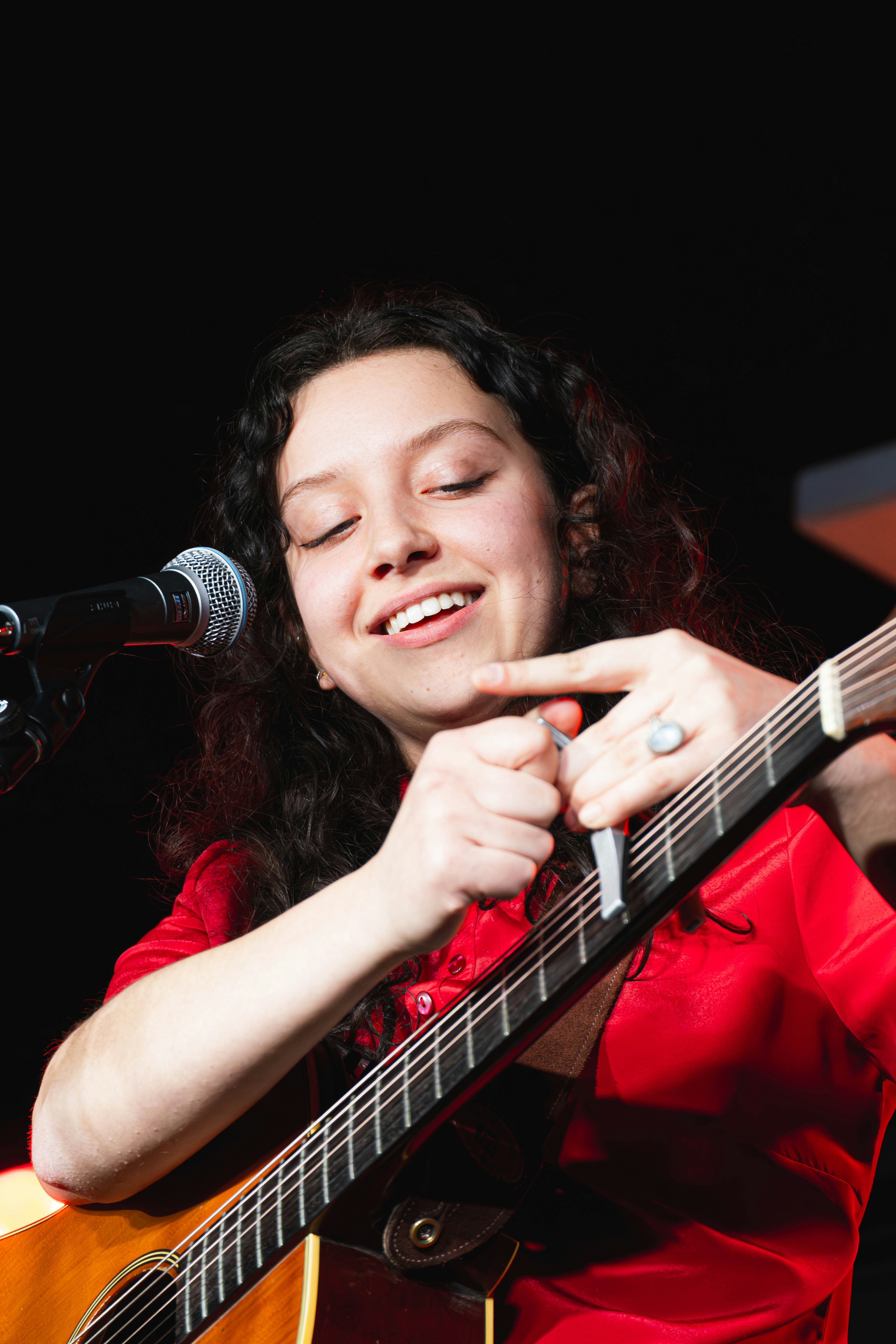 Seorang wanita bermain gitar dan bernyanyi ke mikrofon