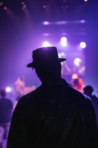 A man in a black jacket and hat standing in front of a crowd