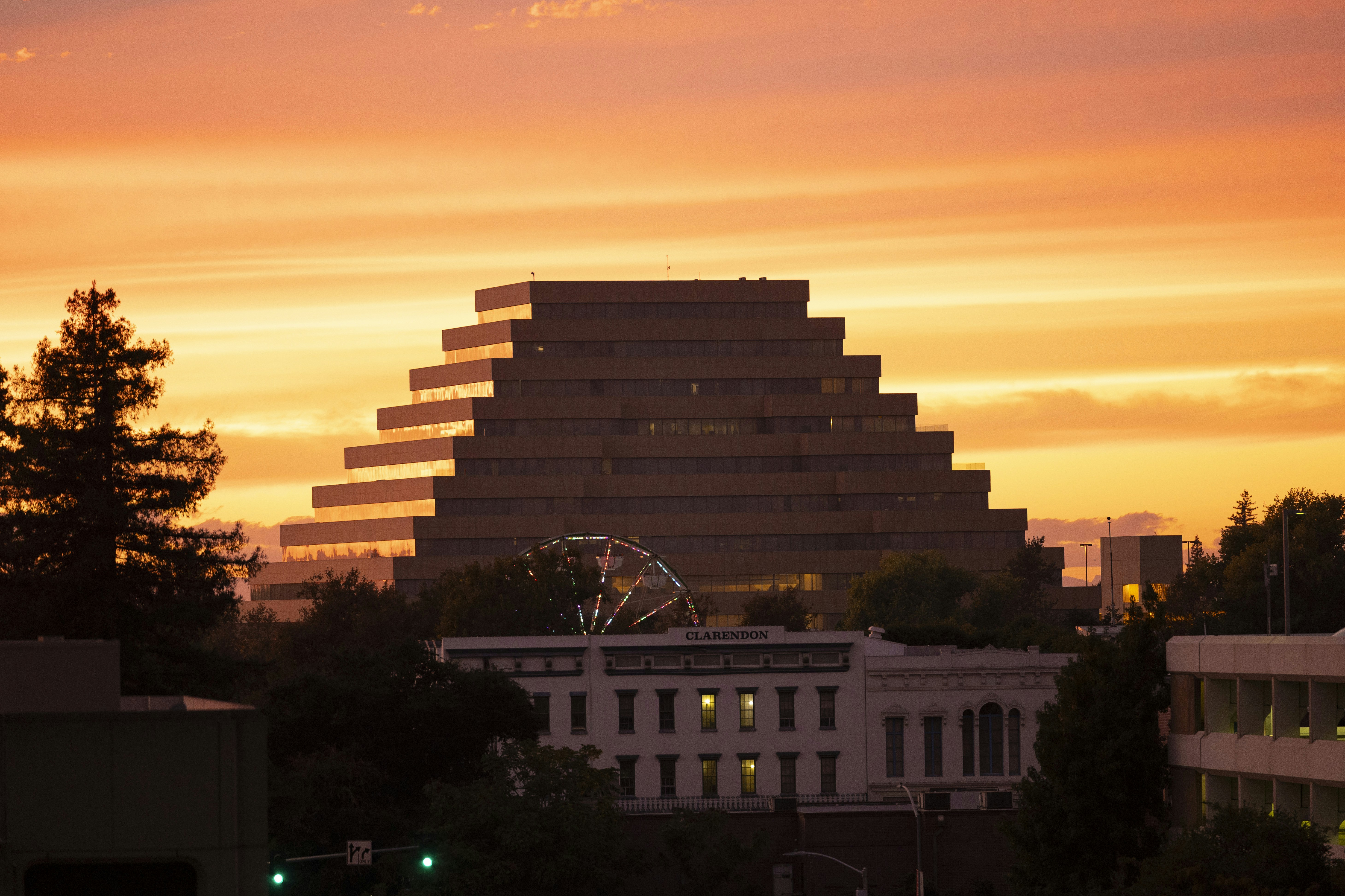 A sunset view of a building with a ferris wheel in the foreground