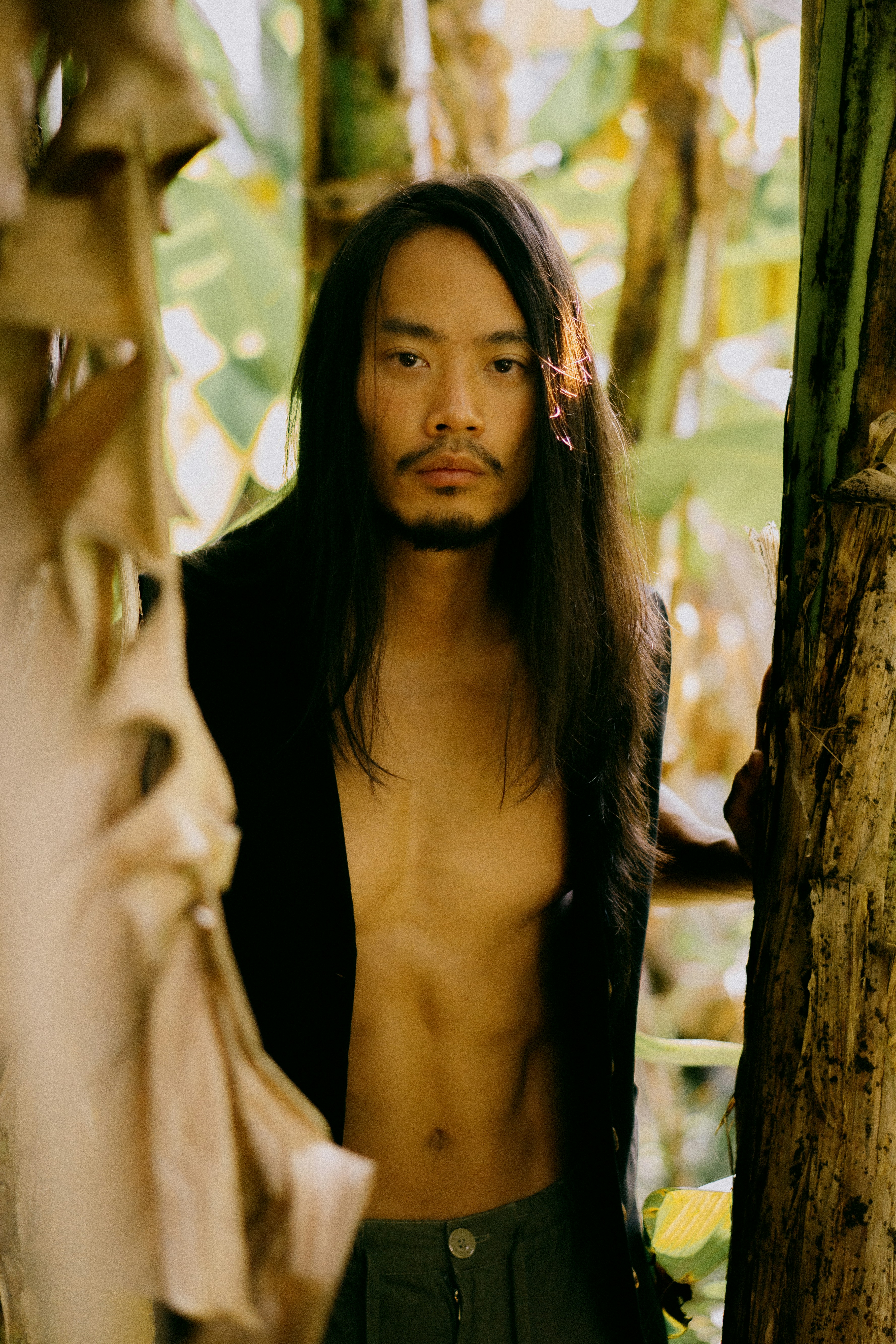 A man with long hair standing next to a tree