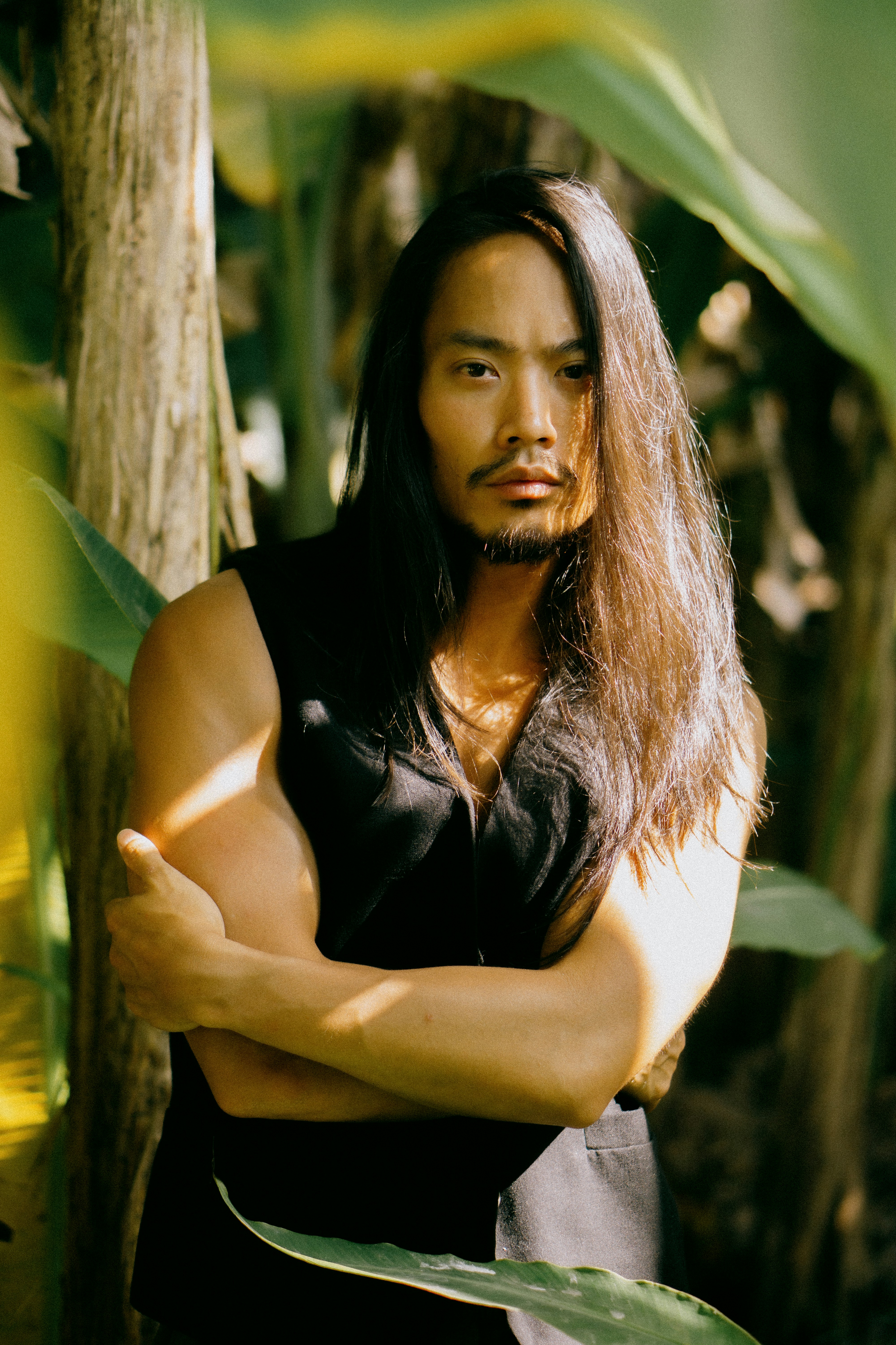 A man with long hair standing in front of a tree