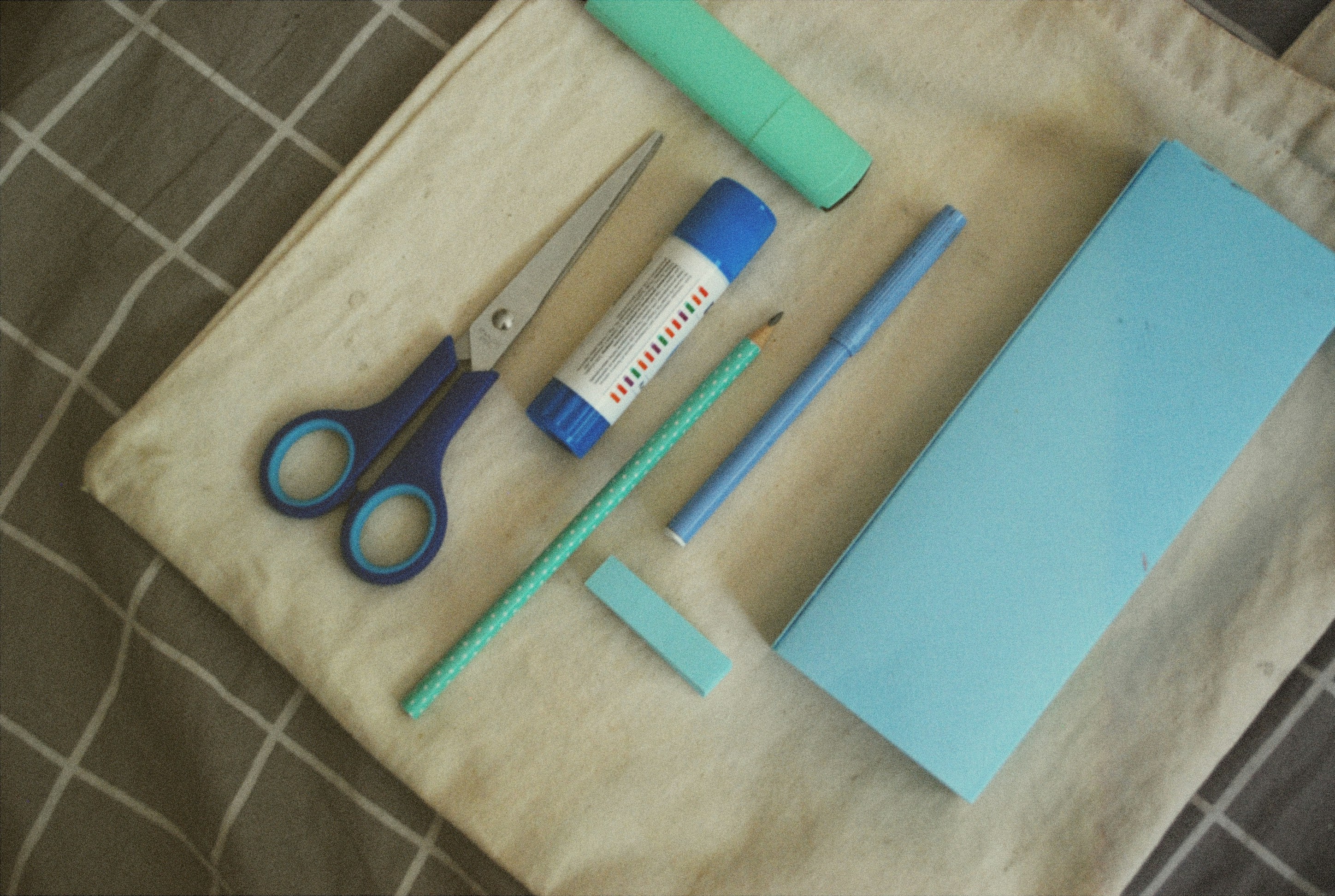 A pair of scissors, a pen, and a notebook on a bed