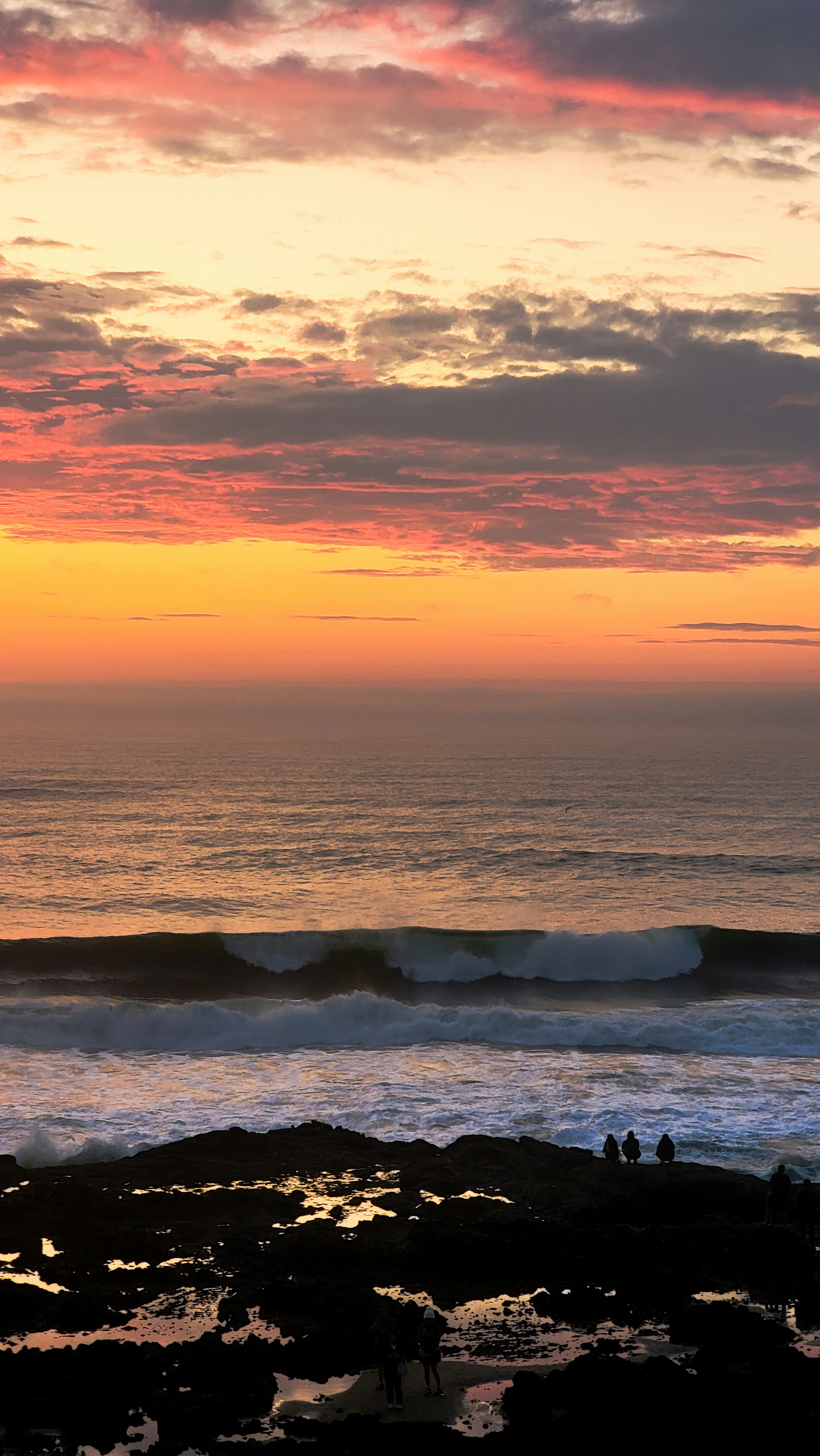 A sunset over the ocean with a surfer on the shore