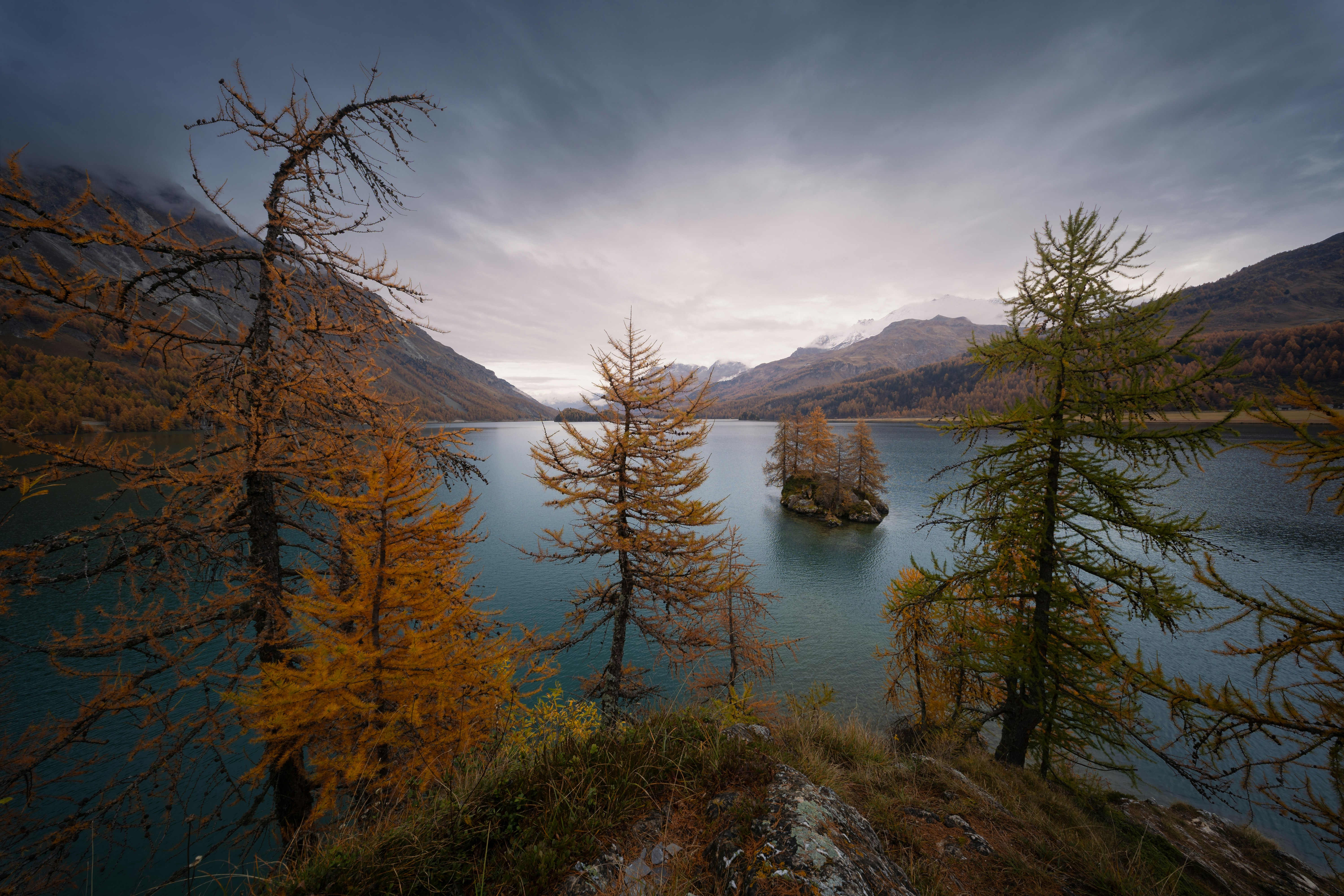 Un lac entouré de montagnes et d’arbres sous un ciel nuageux