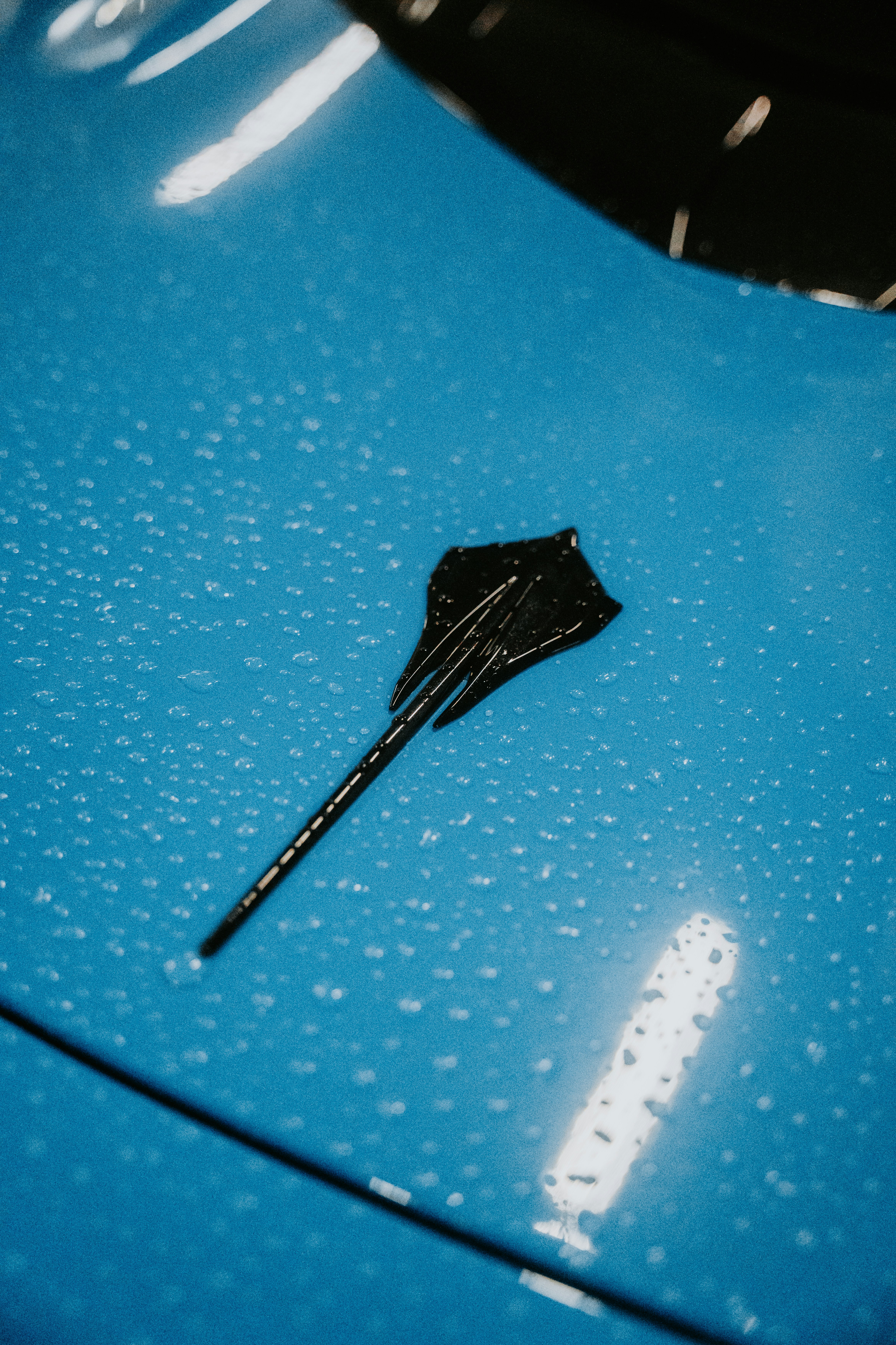 Um close acima de um carro azul com uma vara preta que fura fora dele