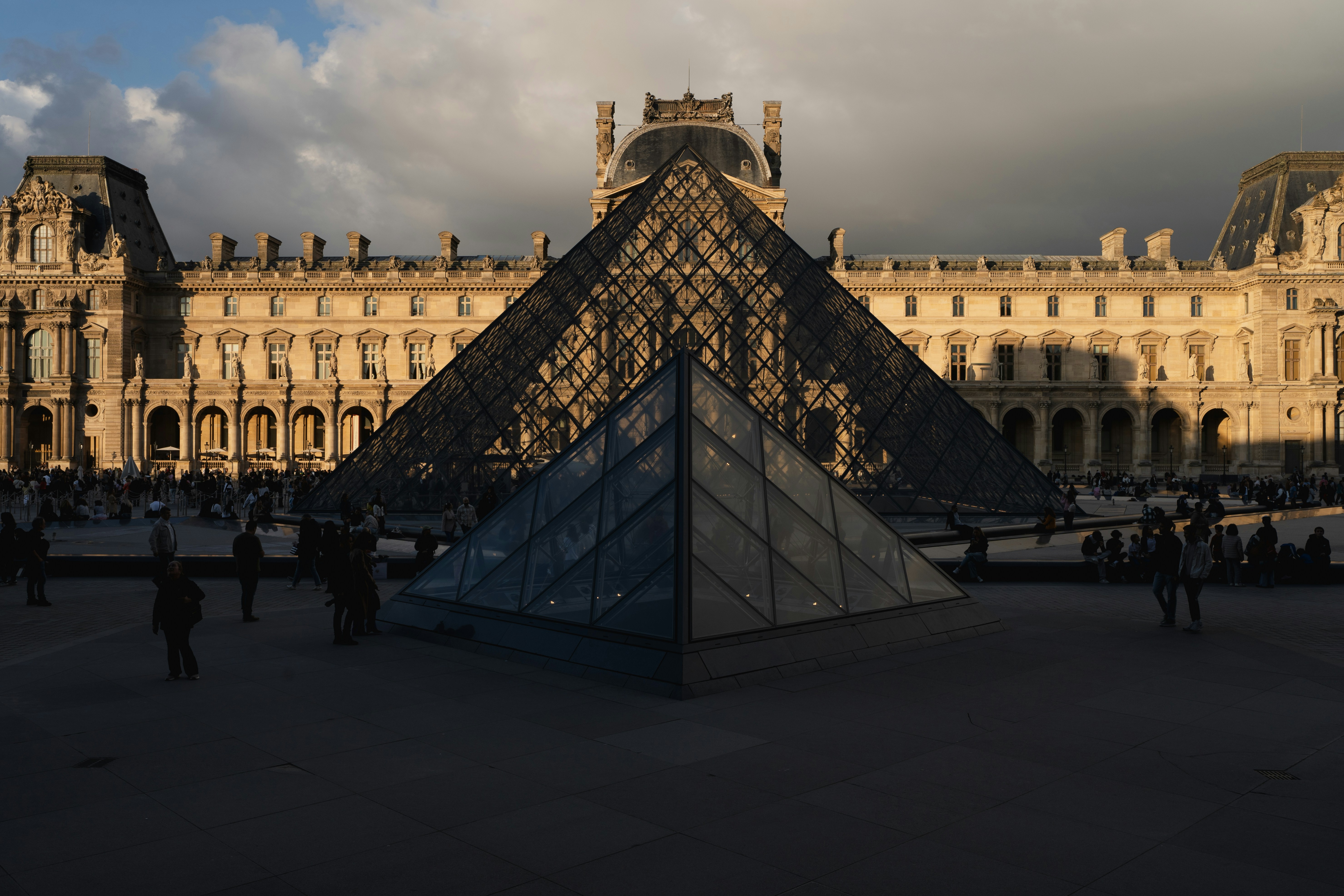Sunset view of the Louvre's glass pyramid with a reflection on the water.