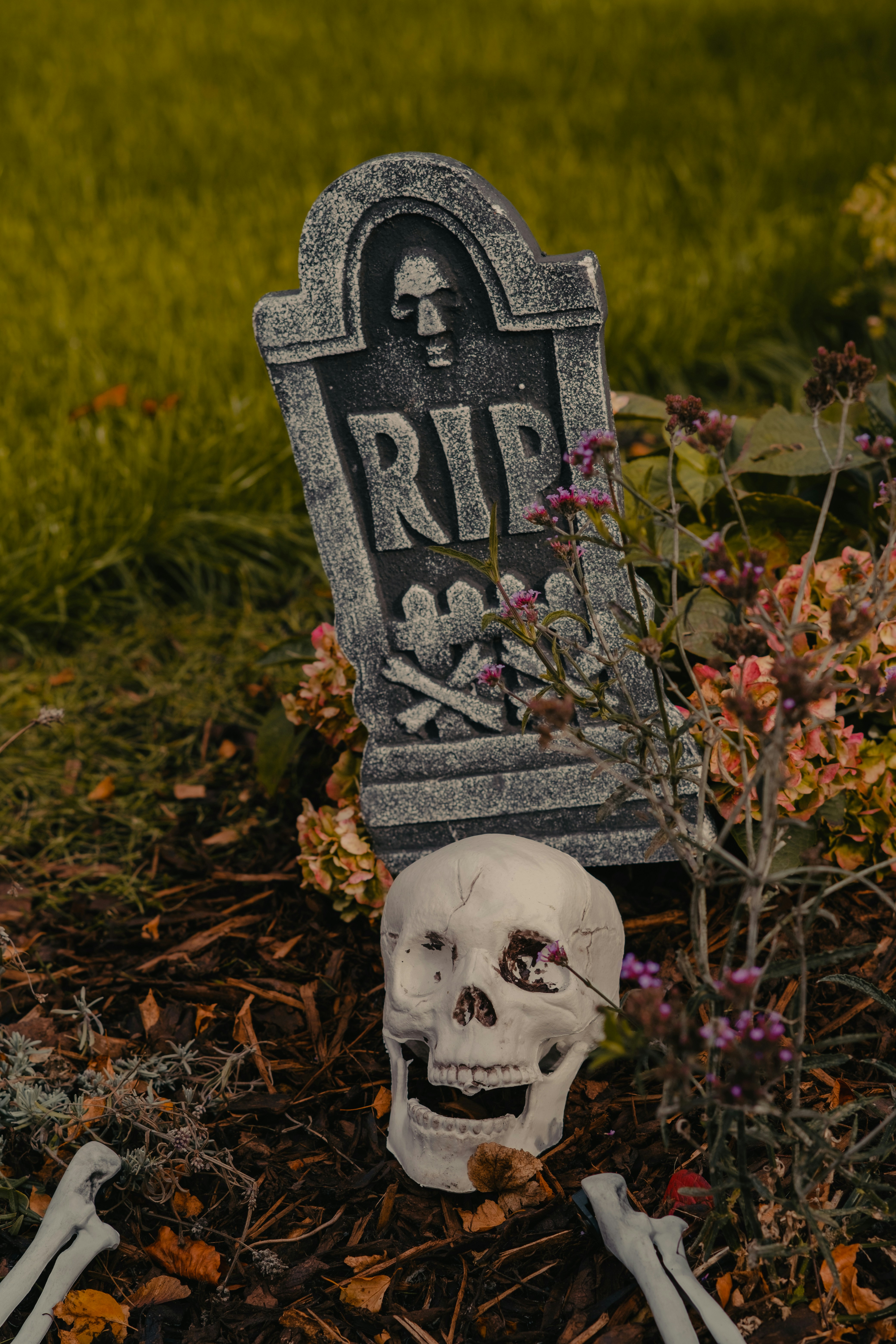 A skeleton sitting in the grass next to a tombstone