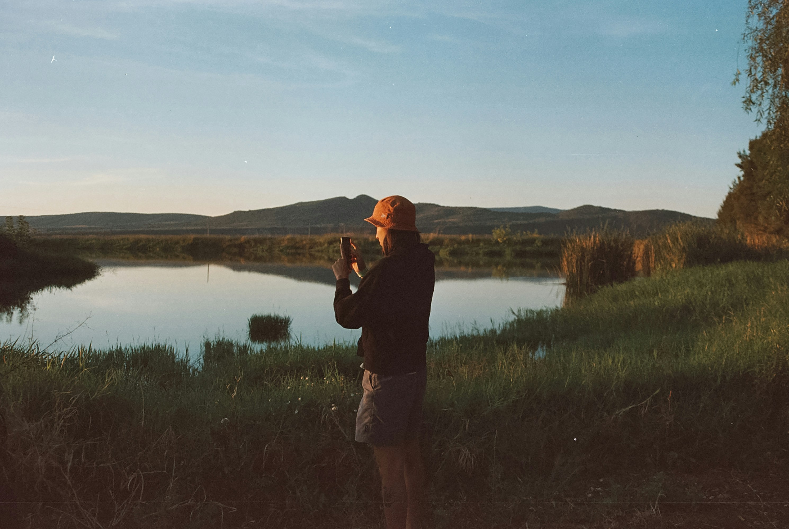 A man standing in a field next to a lake