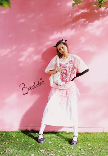 A woman standing in front of a pink wall holding a baseball bat
