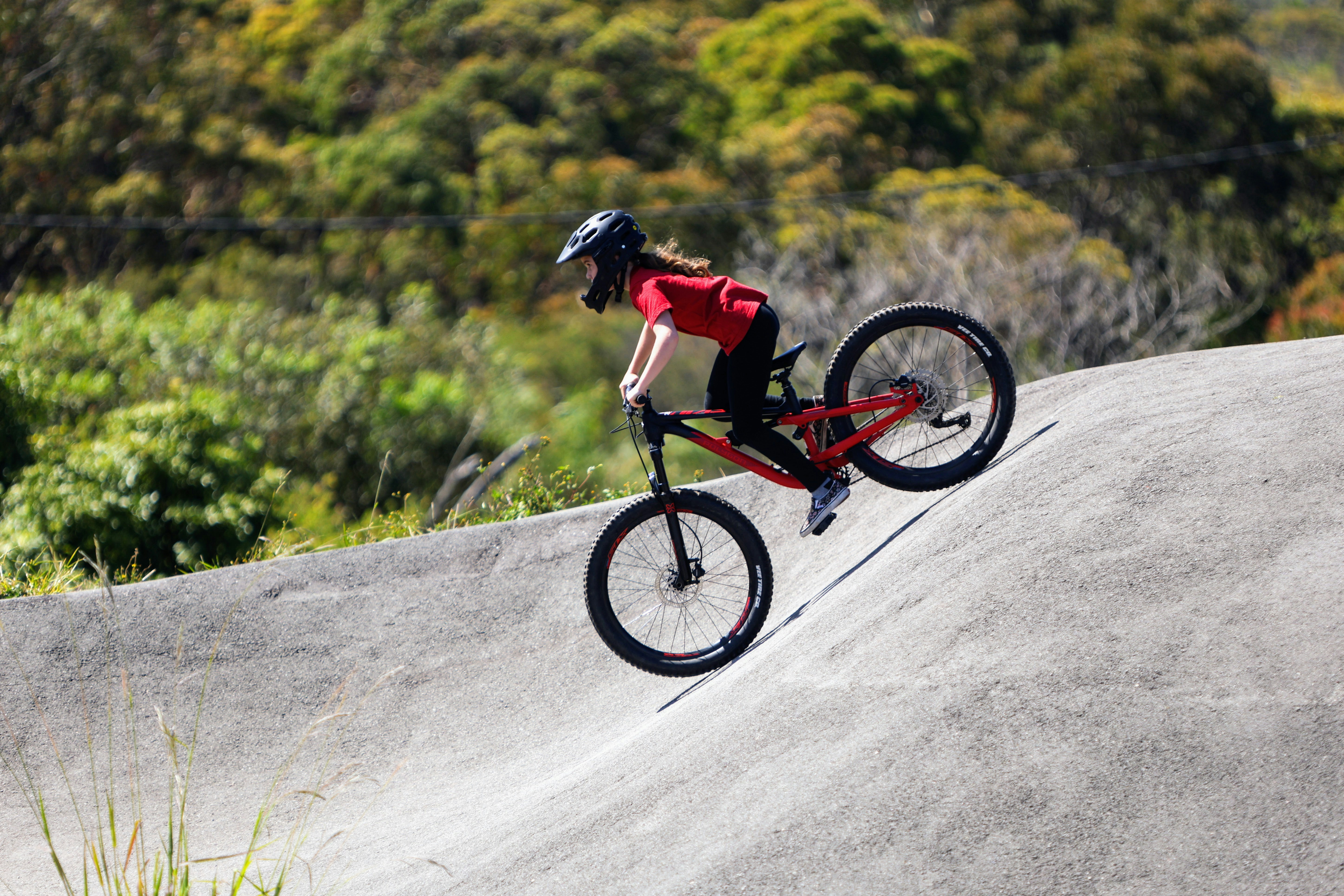 A man riding a bike up the side of a ramp, A girl riding a mountain bike on a pump track.