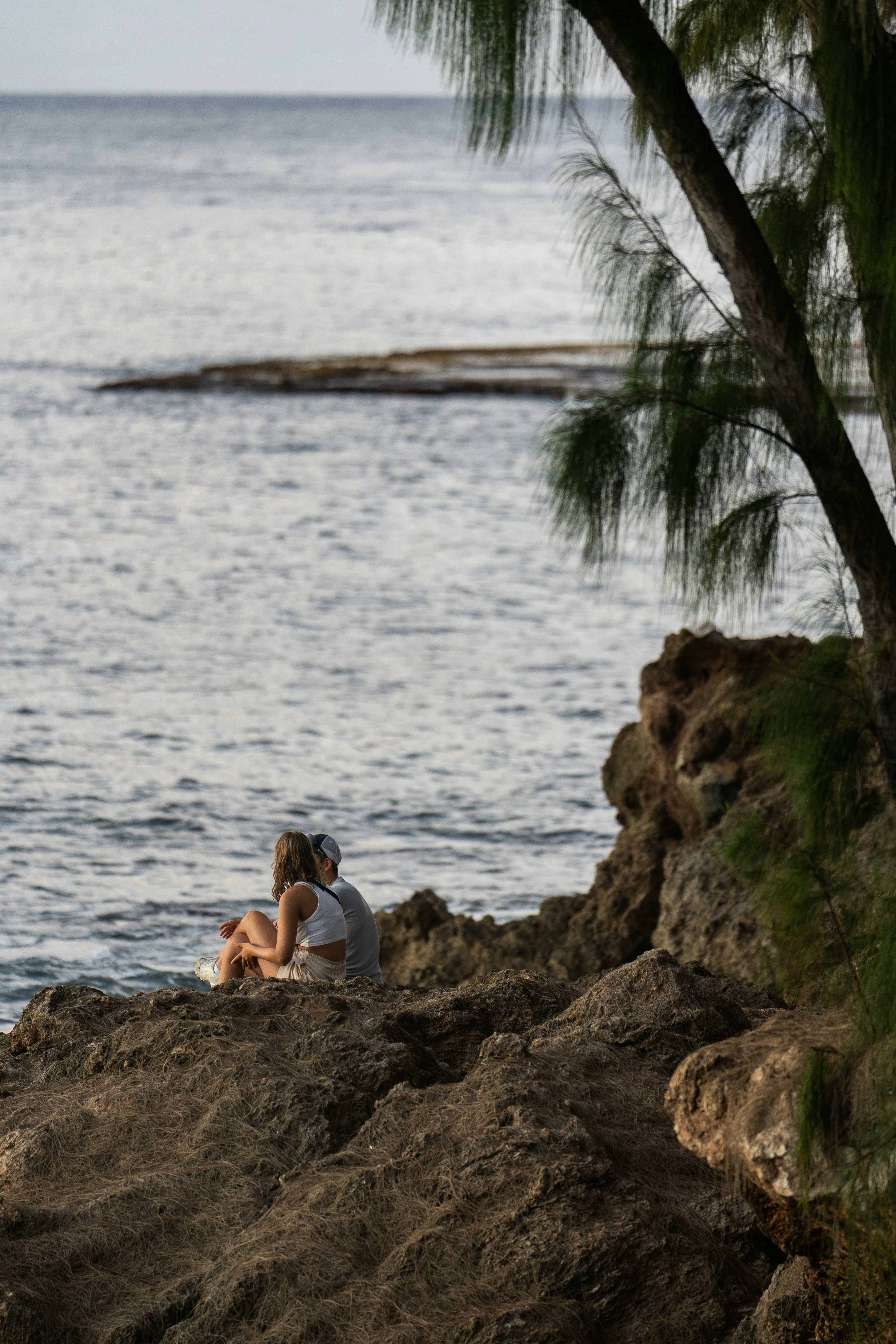 A couple of people sitting on top of a rock near the ocean