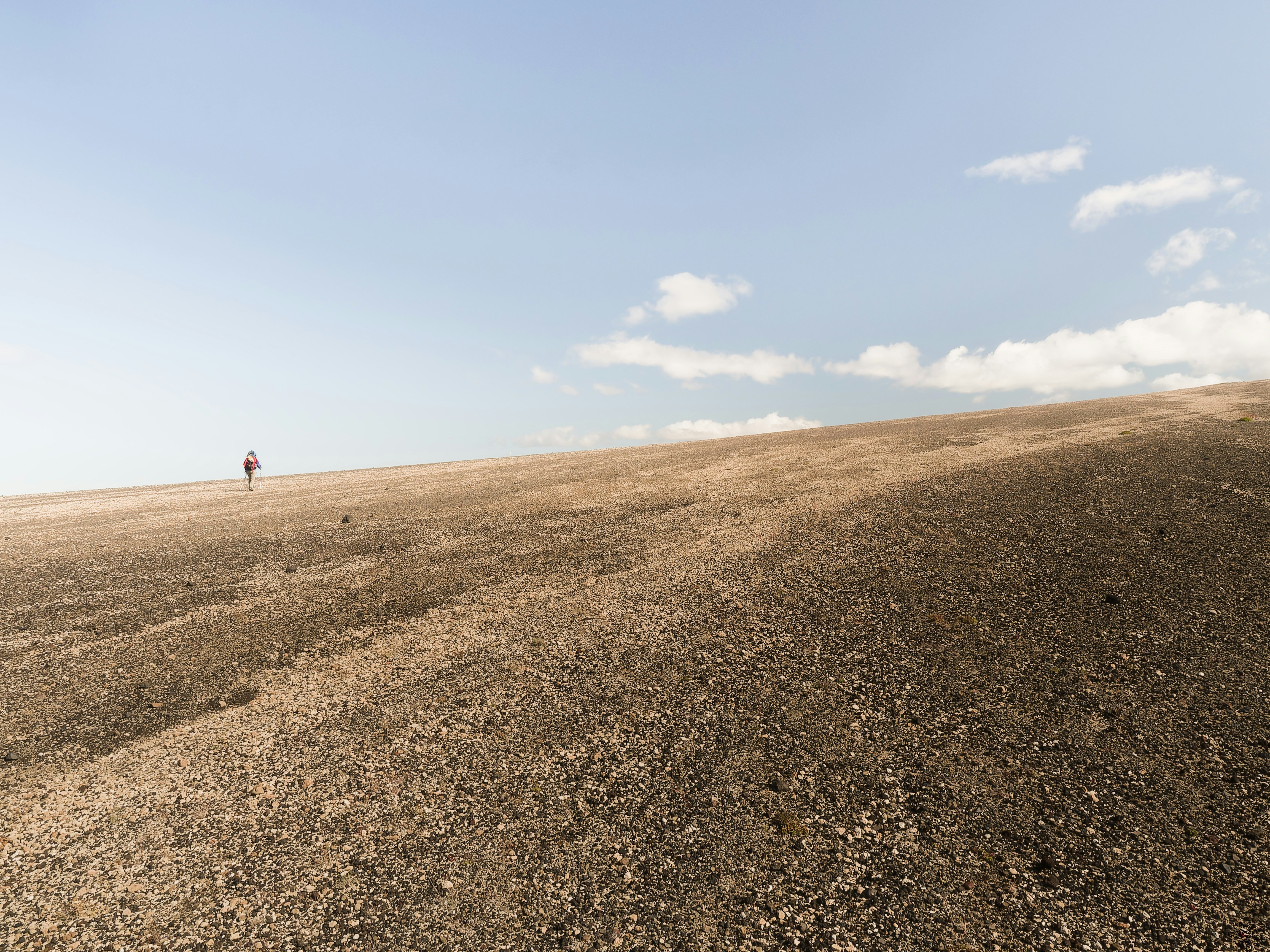 A person walking across a dirt field under a blue sky