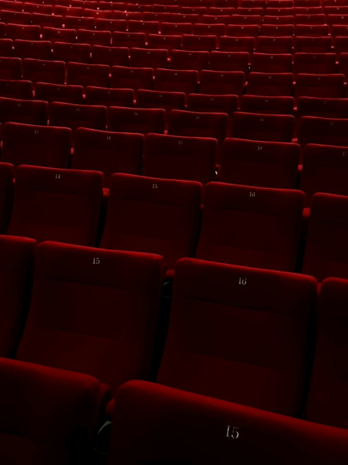Des rangées de fauteuils rouges numérotés dans une salle de cinéma plongée dans la pénombre