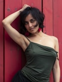 A woman leaning against a red wall with her hand on her head